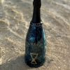 A Chalice Blue Demi-Sec bottle sits on the sand.