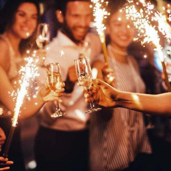 People cheer their champagne glasses while holding sparklers.